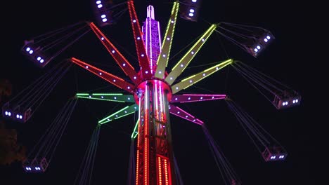 4k video of a swing tower ride, also known as vertical swing and flying tower covered with multicolored led lights spinning on the dark night black sky background.