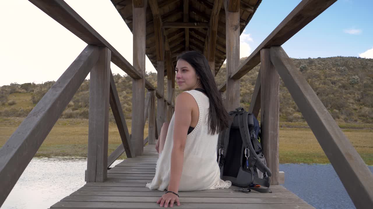 Girl sitting in middle of bridge turns and smiles on windy day, dolly push in