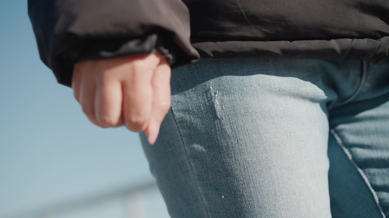 Mano femminile con pugno rilassato e smalto naturale, si muove leggermente su uno sfondo esterno, indossando abiti casual. La scena mantiene condizioni di illuminazione costanti.
