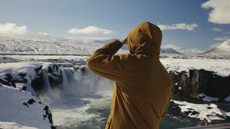 el hombre se acerca a la zona turística de la cascada de godafoss y mira hacia lejos