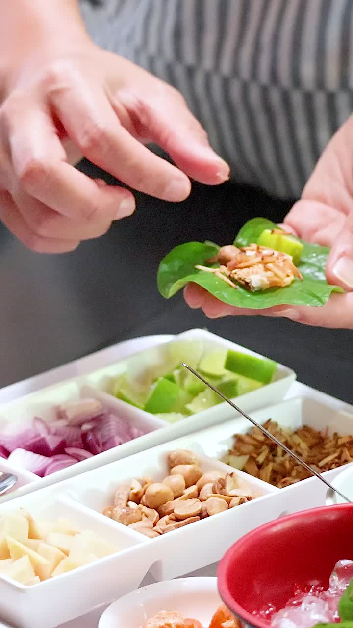 manos montando envolturas tradicionales de hojas de thai miang kham con ingredientes
