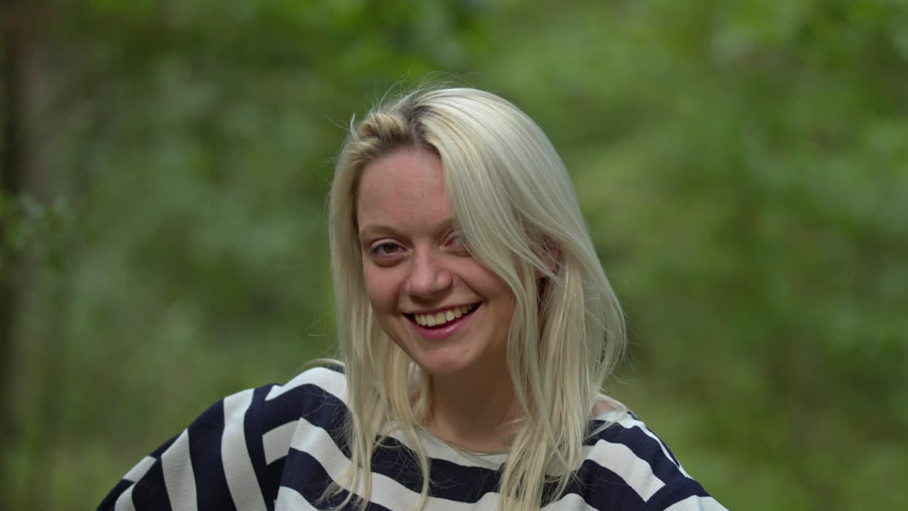 Portret młodej, uśmiechniętej blondynki na tle zielonego parku.