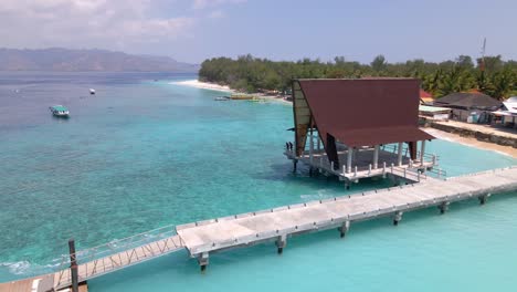 aerial flyover tropical clear water with coral reefs and anchored boats and boathouse in paradise bay