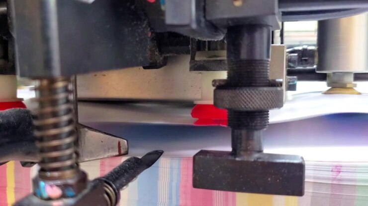 Close-up view of mechanical grippers and suction cups handling paper sheets in a high-speed commercial printing facility.