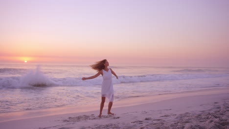 Mujer-Feliz-Libre-Girando-Los-Brazos-Extendidos-Disfrutando-De-La-Naturaleza-Bailando-En-La-Playa-Al-Atardecer-Cámara-Lenta-Dragón-Rojo