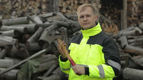 lumberjack in reflective jacket. man woodcutter with small axe. sawn logs, firewood background