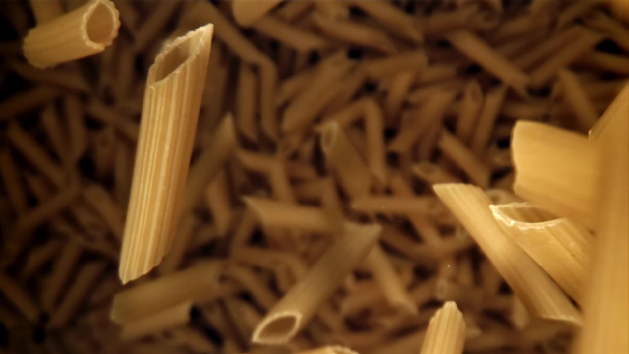 Pezzi di pasta penne cruda che cadono al rallentatore.