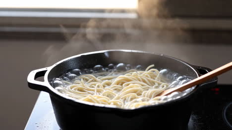 spaghetti being boiled in a pot with a wooden spoon