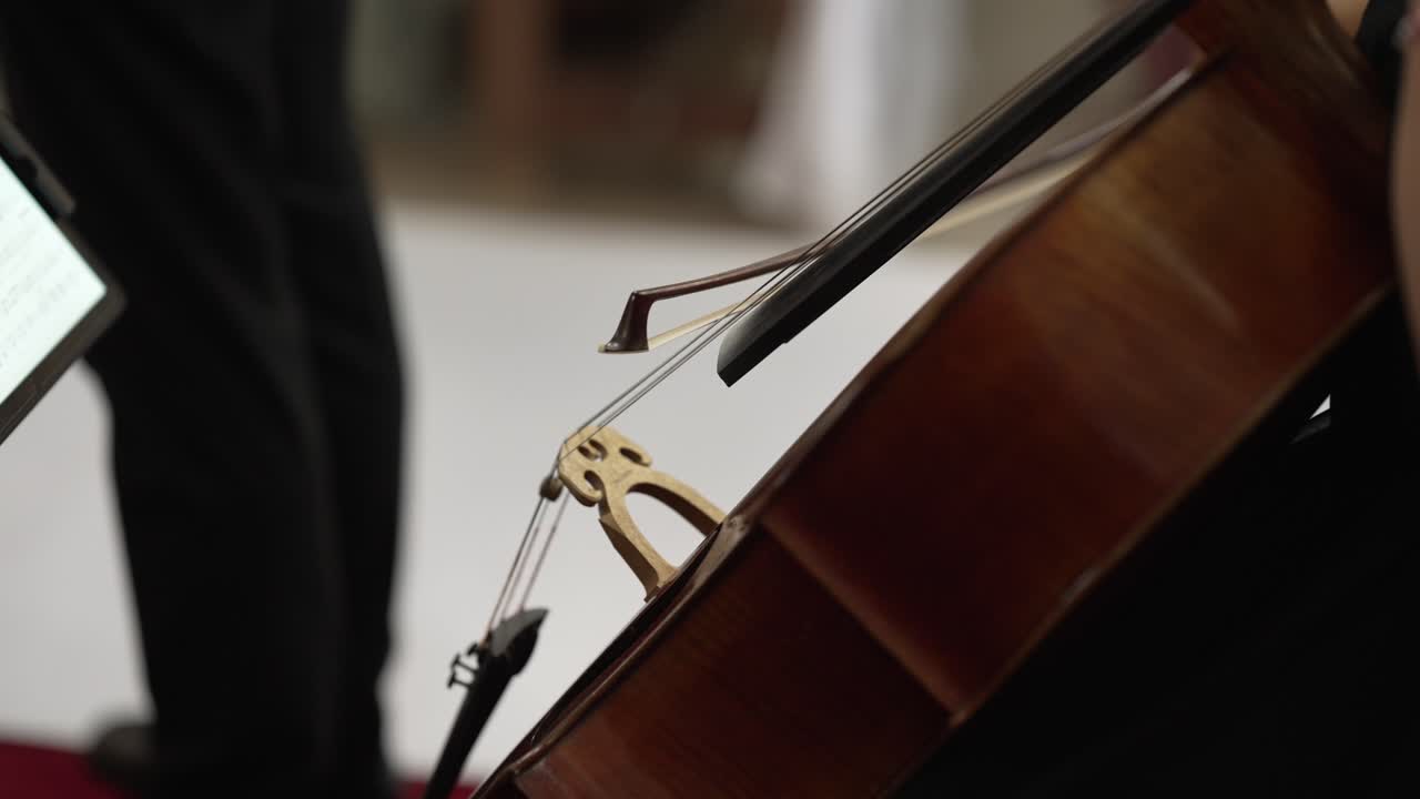 Musician playing cello with bow near sheet music during live classical performance