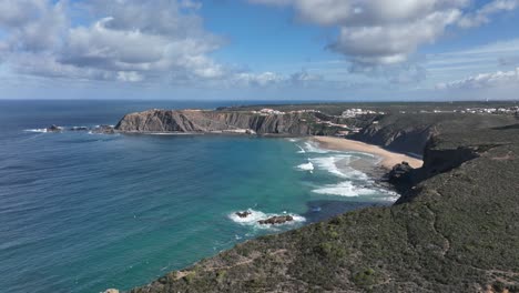 Long-aerial-shot-flying-downwards-above-green-cliffs-surrounding-a-beautiful-bay-by-the-ocean