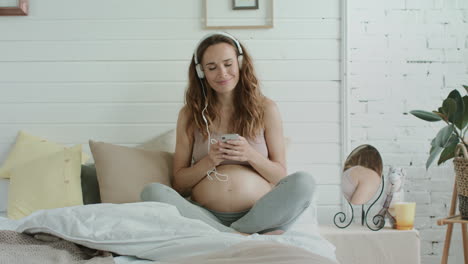 Smiling-pregnant-woman-listening-music-in-bed.-Expectant-mother-resting-indoors