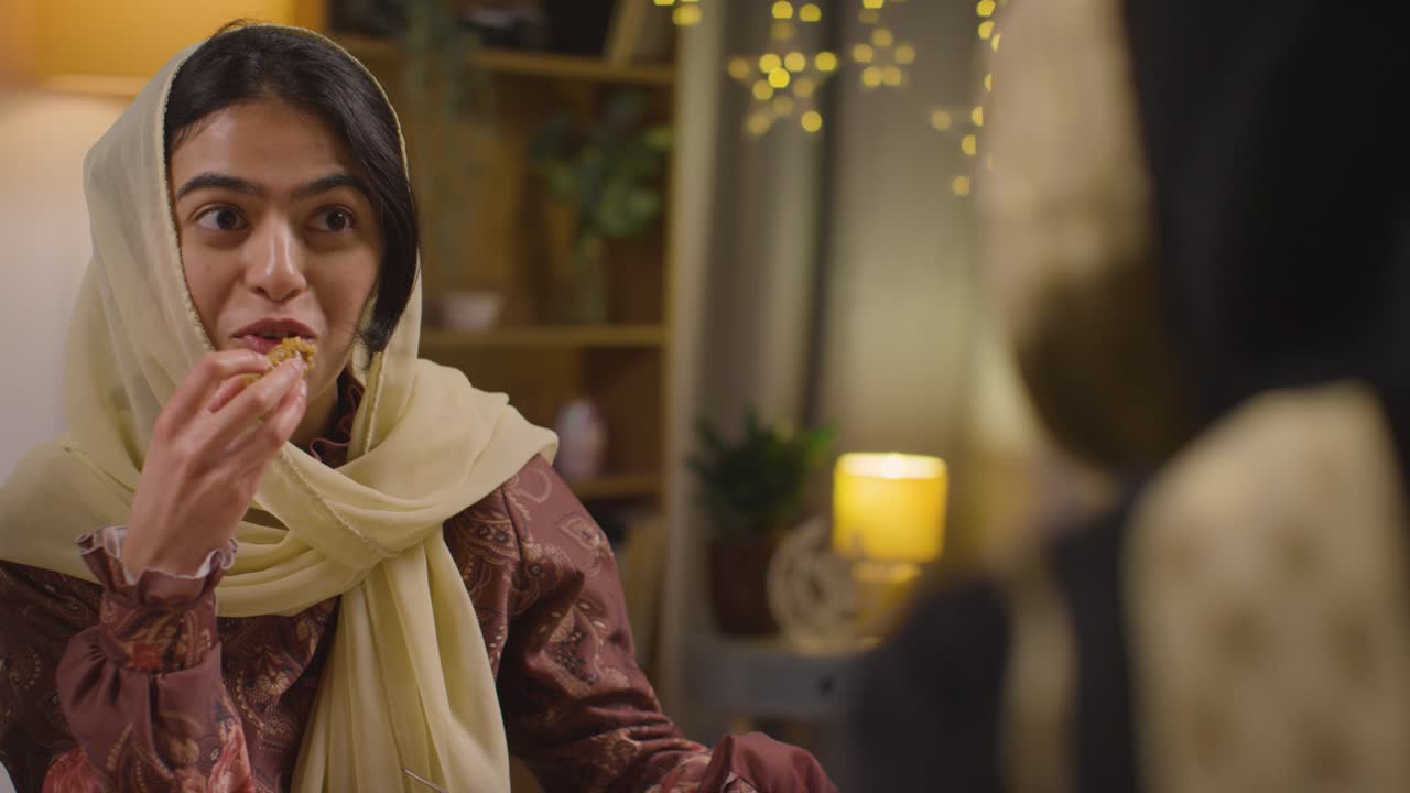 familia musulmana sentada alrededor de una mesa en casa comiendo para celebrar el eid 2