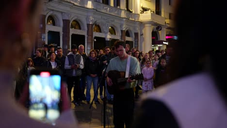 street musician plays guitar to a crowd at night