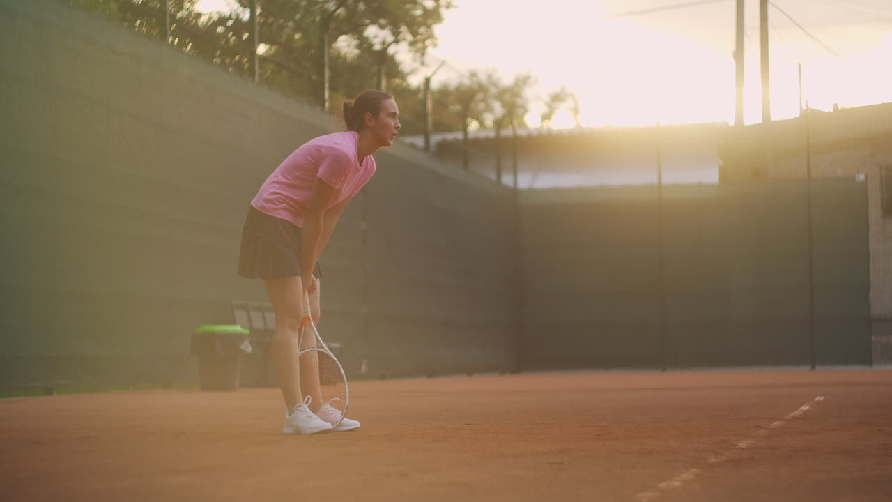 소녀는  ⁇  표면의 개방된 코트에서 테니스 훈련을 하는 동안 피곤하고 라켓에 기대어 있습니다.