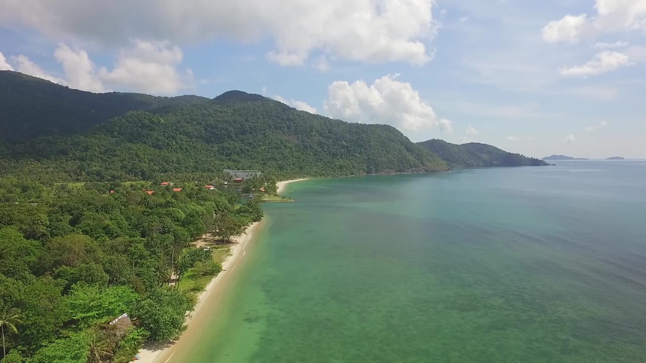 Aerial side tracking shot of a long white sand beach on Koh Chang with Jungle, sea view and bungalow resorts