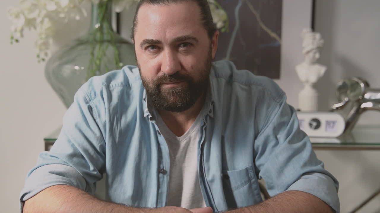 бородатый мужчина терпеливо выносит долгий разговор женщины, глядя в камеру