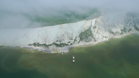 Top-down-distant-view-Beachy-Head-Lighthouse,-white-cliffs,-foggy-sky-and-sea-taken-by-dji-mini-3-pro-drone-in-Eastbourne-England