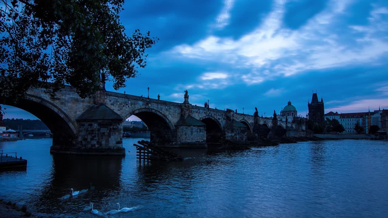 Zeitrafferaufnahme am blauen Morgen der Karlsbrücke in Prag, Tschechische Republik, neben dem Fluss Moldau mit Panoramablick auf das Flussufer