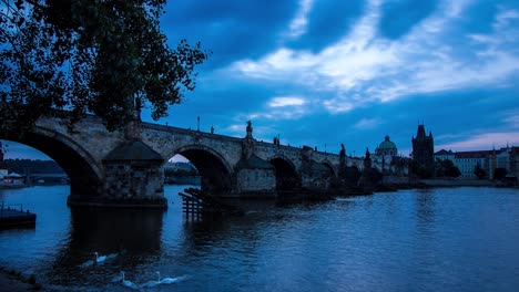 blue morning timelapse of the charles bridge in prague, czech republic next to the vltava river with panoramic view of the river shore