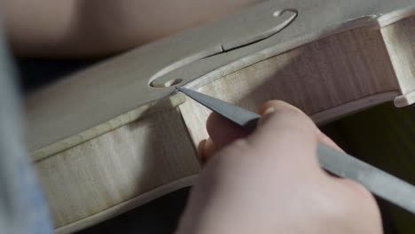 macro close up of artisan luthier maker work on new classic handmade raw violin smooth edge in waist and purfling rasp in workbench of workshop in cremona italy 4k video