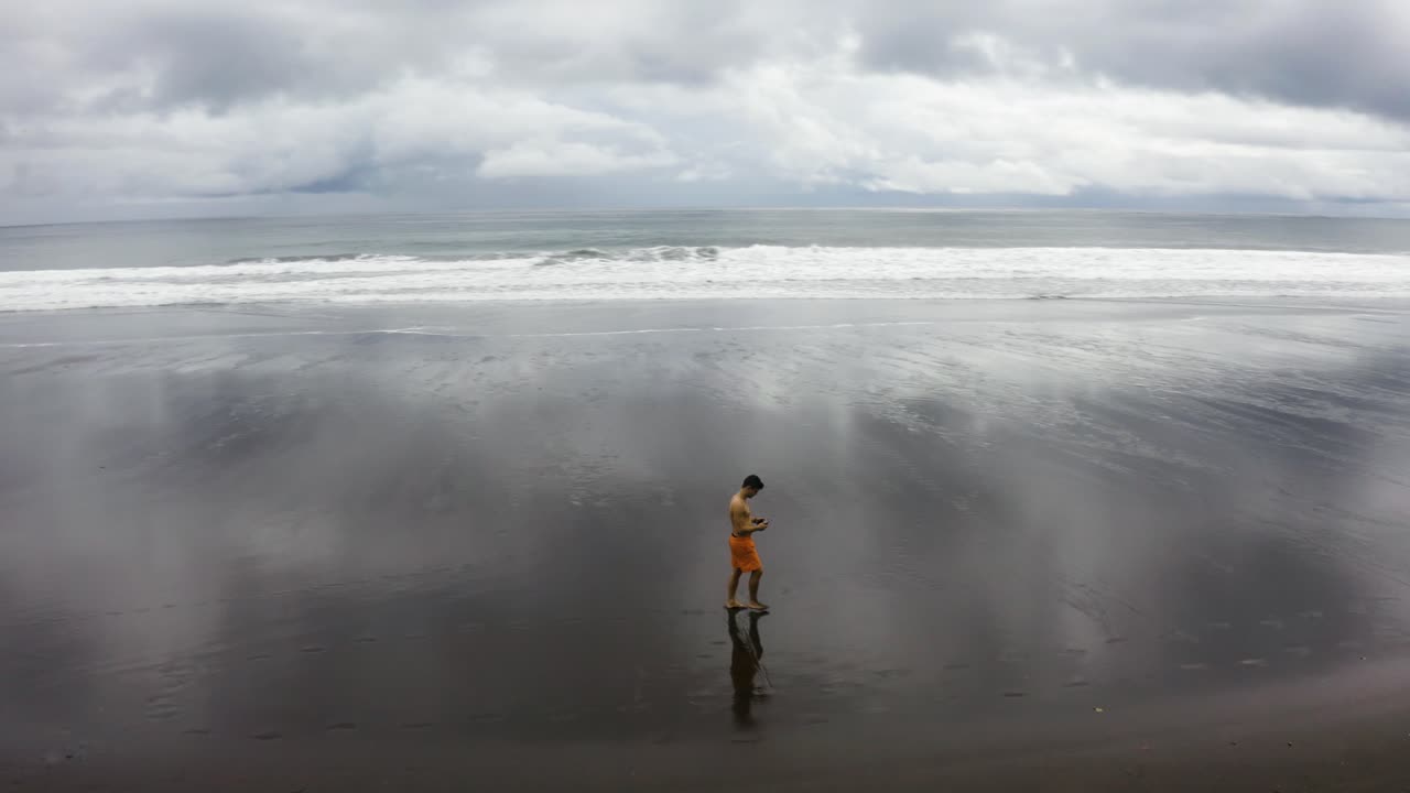 Ripresa aerea di un giovane uomo che cammina su una spiaggia deserta, Colombia.