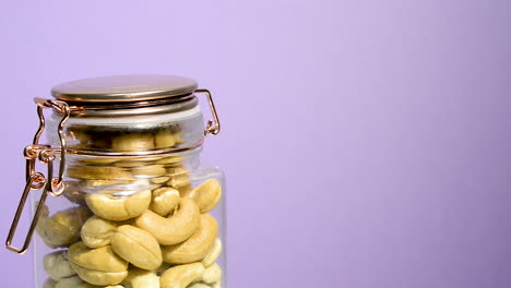 Close-up-of-an-airtight-mason-jar-rotating-with-toasted-cashew-nut-on-a-neon-lilac-background
