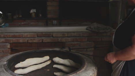 una mujer panadera con turne horneando un shotis puri o shoti georgiano tradicional