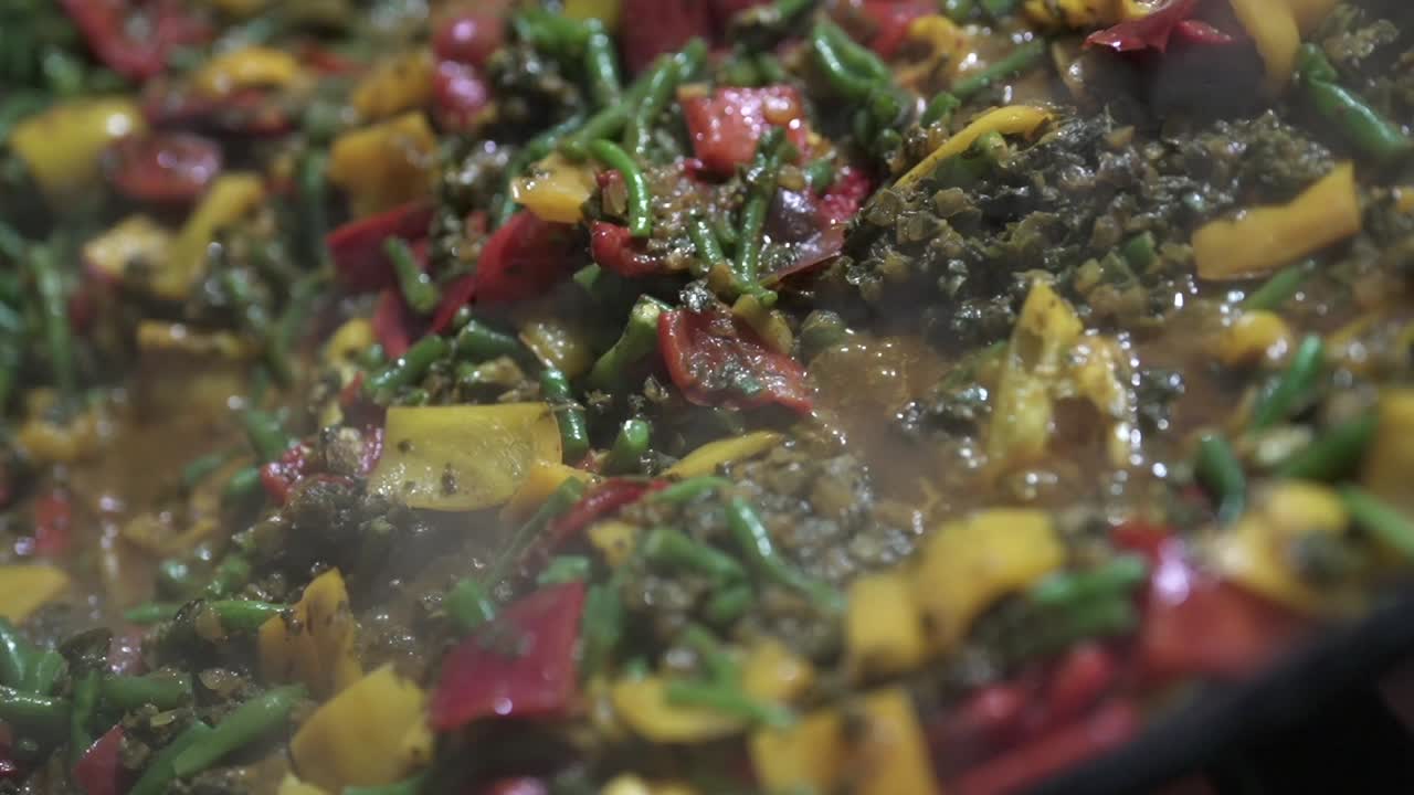 Smoking and bubbling vegan risotto simmers as fresh vegetables soften and blend in the pan, shown in extreme close-up with a slow-motion pan shot