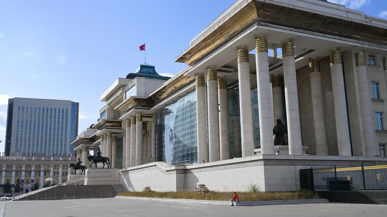 Side view of the Government Palace building with the towering Mongolian flag at Sukhbaatar Square in Ulaanbaatar, Mongolia, with the Genghis Khan statue placed at its front center.