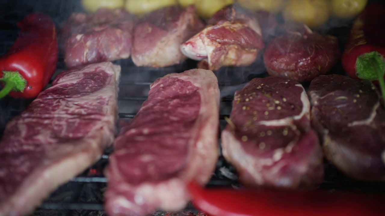 Carne che cuoce su una griglia con melanzane e peperoni rossi, con del fumo che sale