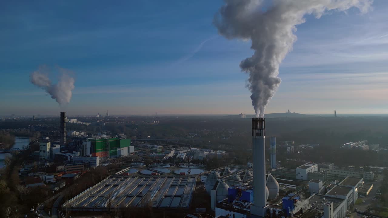 Impianto di termovalorizzazione dei rifiuti urbani con grandi ciminiere che emettono vapore in un cielo azzurro, che illustra lo sviluppo urbano sostenibile. Fantastica panoramica aerea con drone