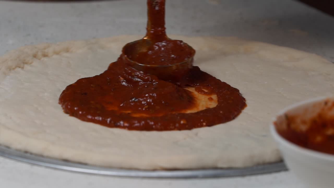 spread pizza souse on the pizza base closeup