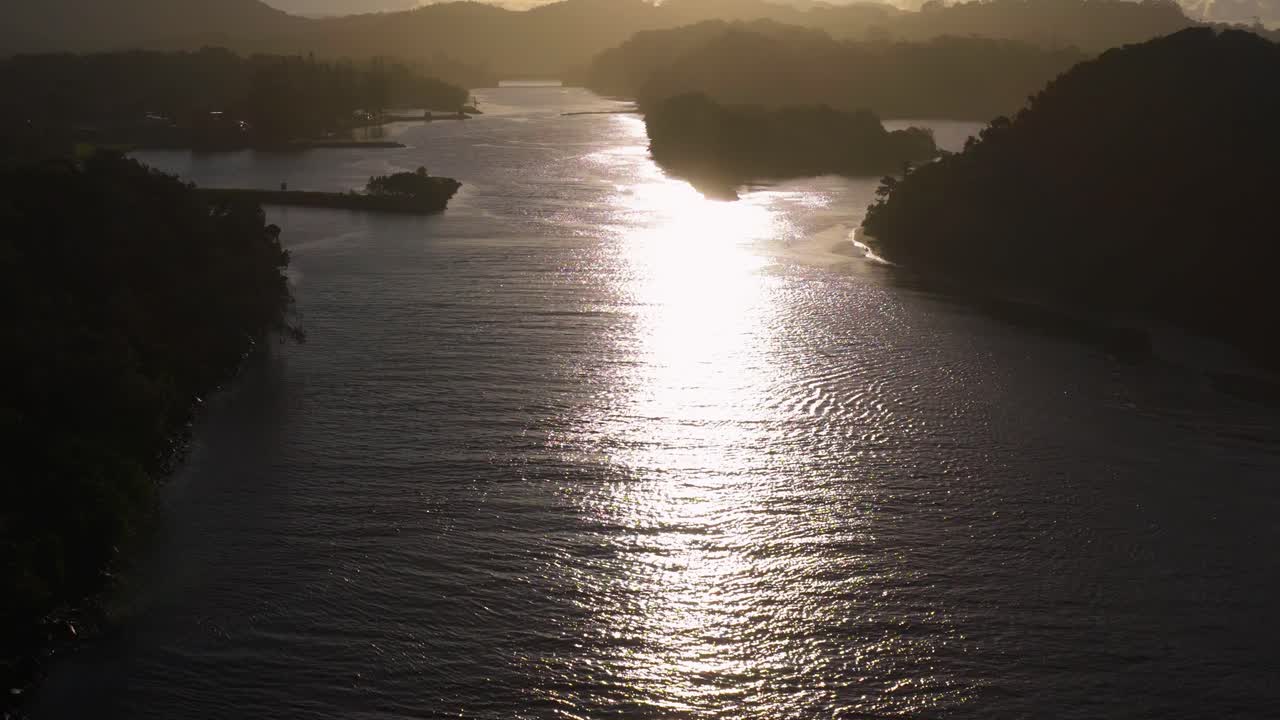 Aerial view of a serene river at sunset in Brunswick Heads, NSW, capturing the golden reflection on water and surrounding landscape