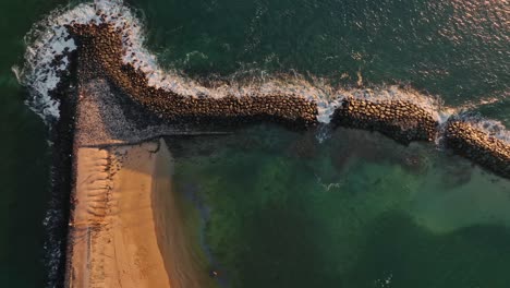 a birds eye view of a breakwater stopping waves at golden hour