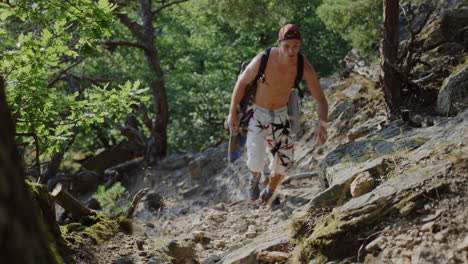 caucasian-young-man-hiking-a-mountain-trail-bare-chest,-snapback-hat,-mountaineer-gear,-climbing-outdoors,-looking-around-for-a-wall-to-climb,-sunny-summer-weather-in-Austria,-Durnstein,-Europe