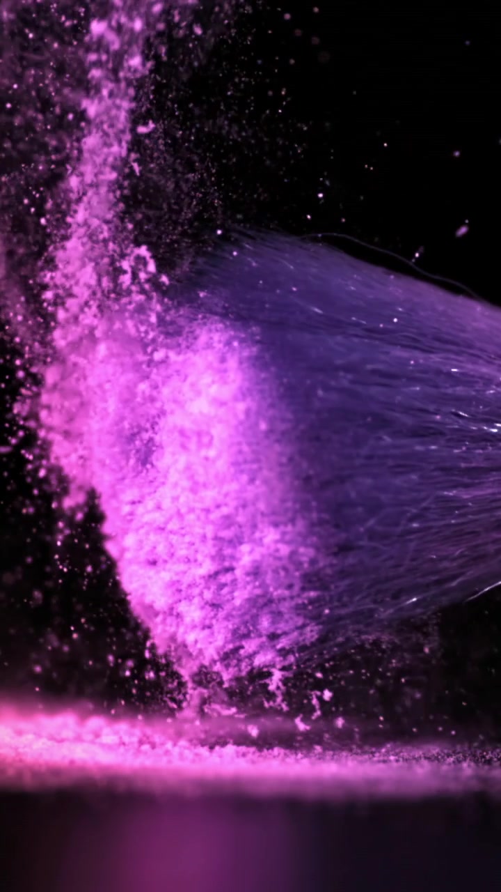 Polvo vibrante rosa y morado dispersándose sobre un fondo negro a cámara lenta