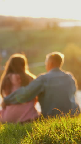 romantic couple rests in nature. young people boy and girl sitting together on grass and looking at sunset. couple in love on date outdoors. vertical video