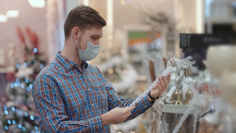 A-man-in-a-protective-mask-in-a-jewelry-store-and-garlands-with-toys-for-Christmas-trees-and-at-home.-Christmas-garlands-and-decor