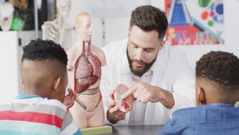 Vielfältiger-Männlicher-Lehrer-Und-Glückliche-Schulkinder,-Die-Im-Biologieunterricht-Das-Modell-Des-Menschlichen-Körpers-Studieren