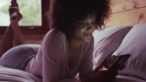 mujer de raza mixta usando un teléfono inteligente en el dormitorio