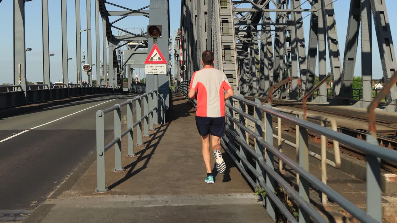 Male trail runner running towards and on steel bridge between train tracks and asphalt road