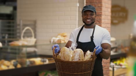 portrait of a happy man in a black cap and white t-shirt in a black apron who holds in his hands a large basket of pastries in a modern grocery store