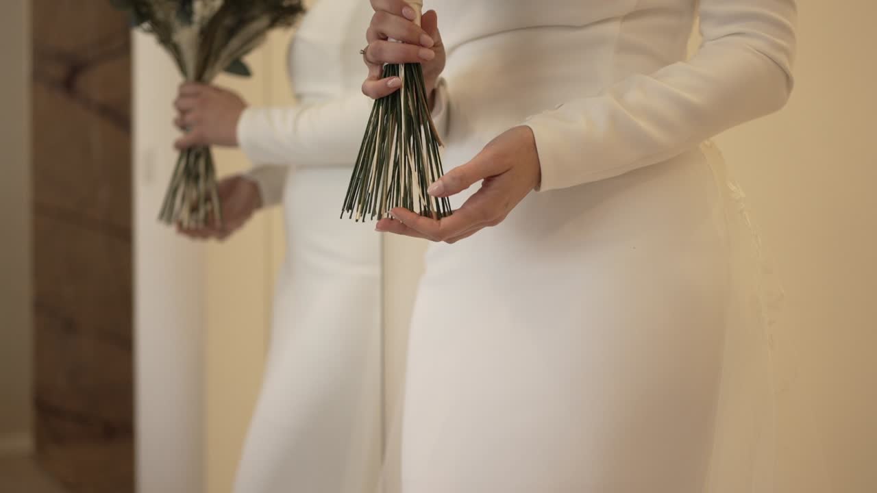 bride, in a fitted white gown, holds a simple, elegant bouquet, reflected in a mirror