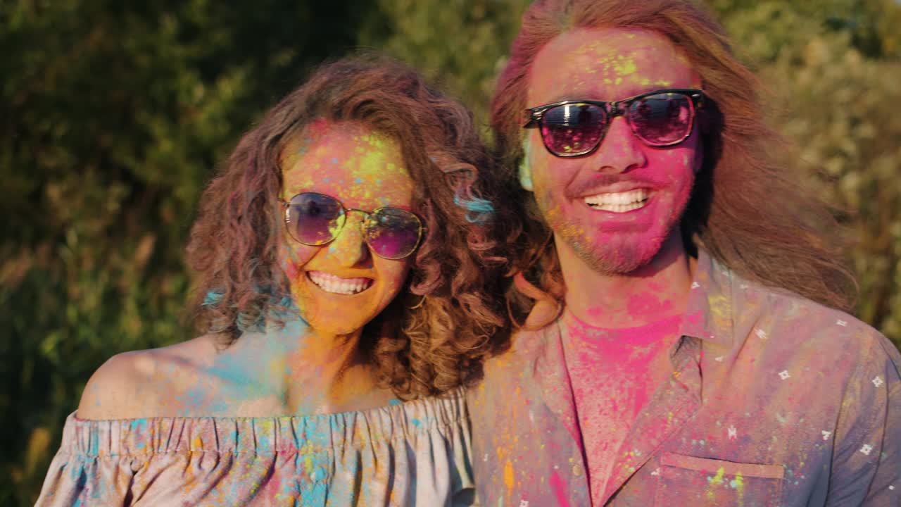 Gioiosa donna asiatica che abbraccia una coppia felice coperta di polvere colorata e sorridente al festival Holi.