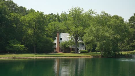 picturesque view of a charming white farmhouse situated across a tranquil lake, framed by the natural beauty of lush trees