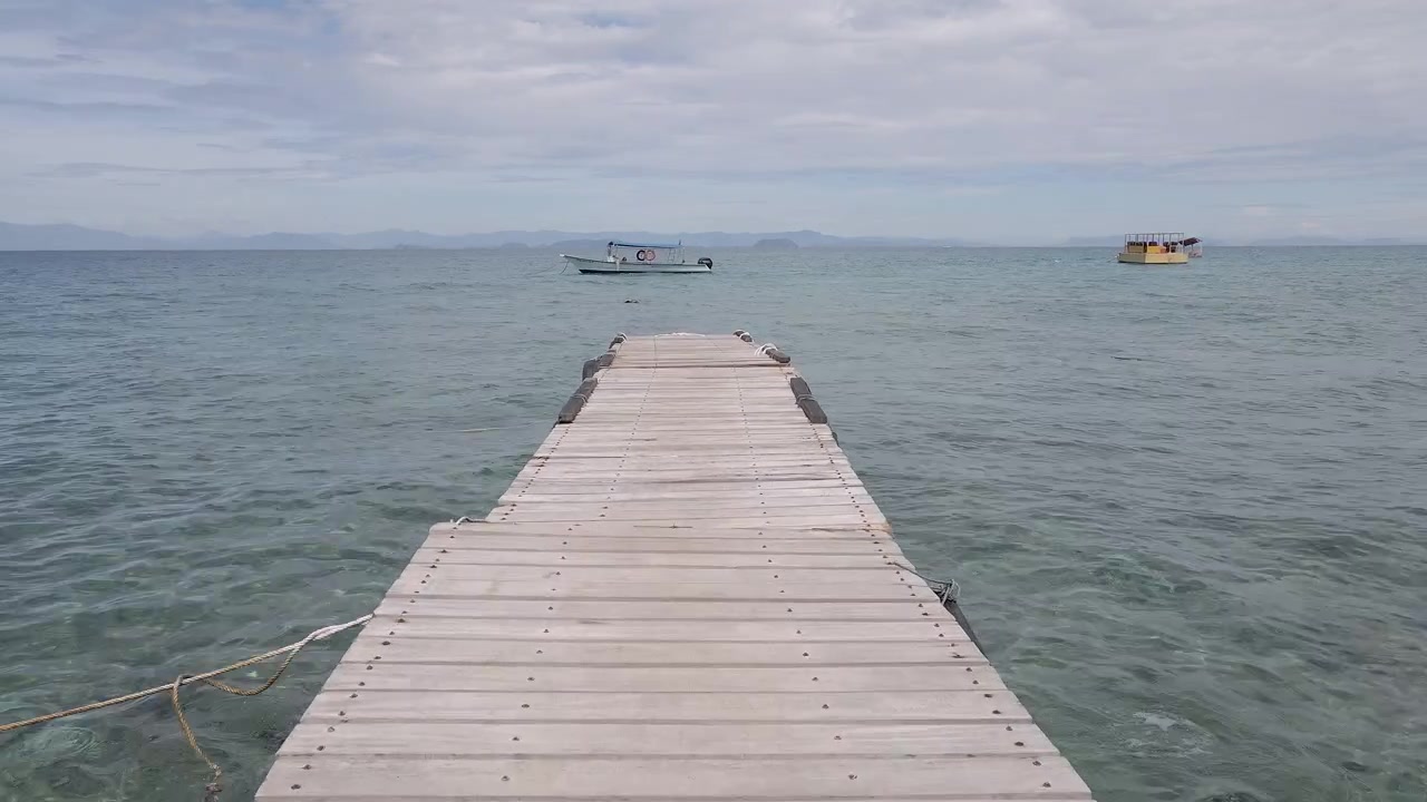 Vista aérea moviéndose a lo largo de un muelle flotante sobre el océano hacia barcos distantes. Toma de dron con efecto dolly en un resort remoto, mar de China Meridional, Malasia.