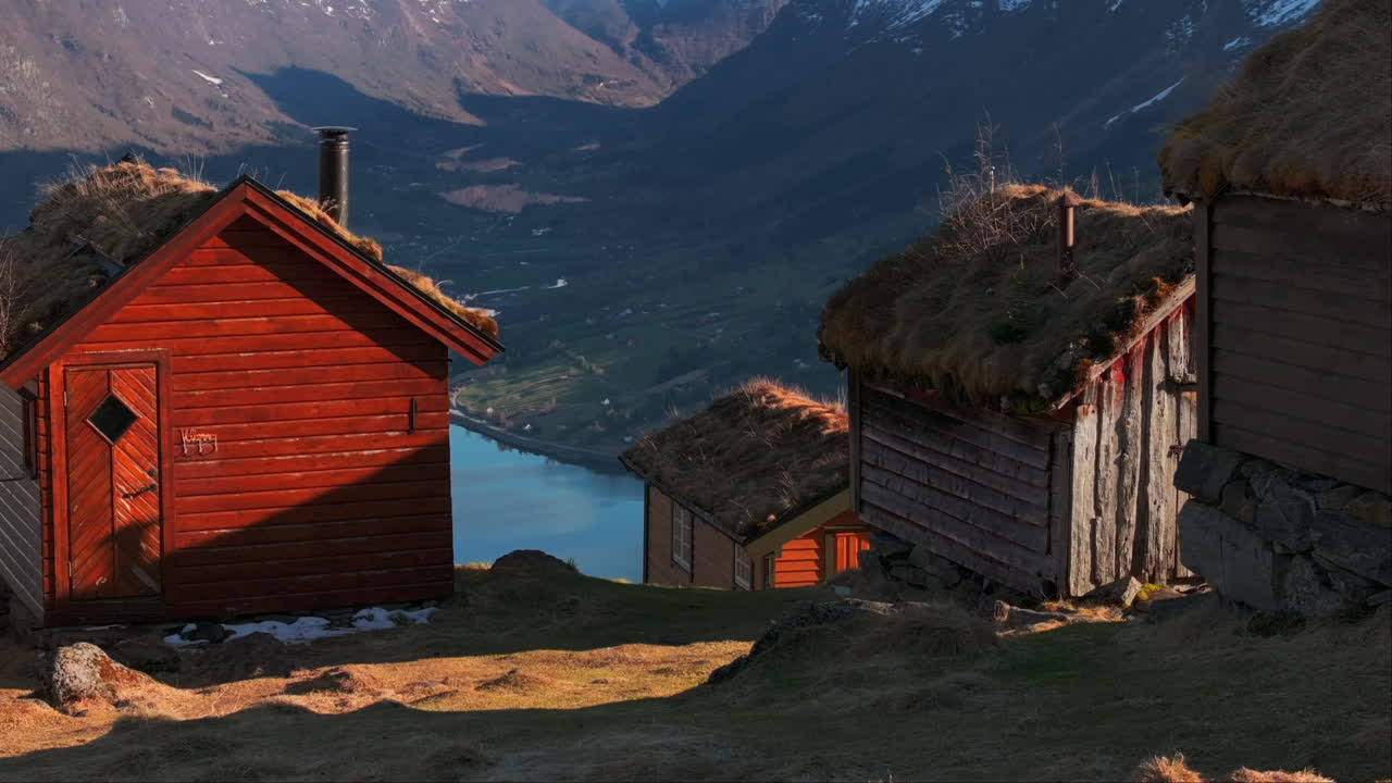 Idyllic Norway mountainside cabins in sunset overlook Olden valley fjord; drone