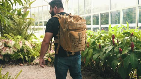 young male traveler with backpack walks through a tropical glass metal greenhouse handheld shot