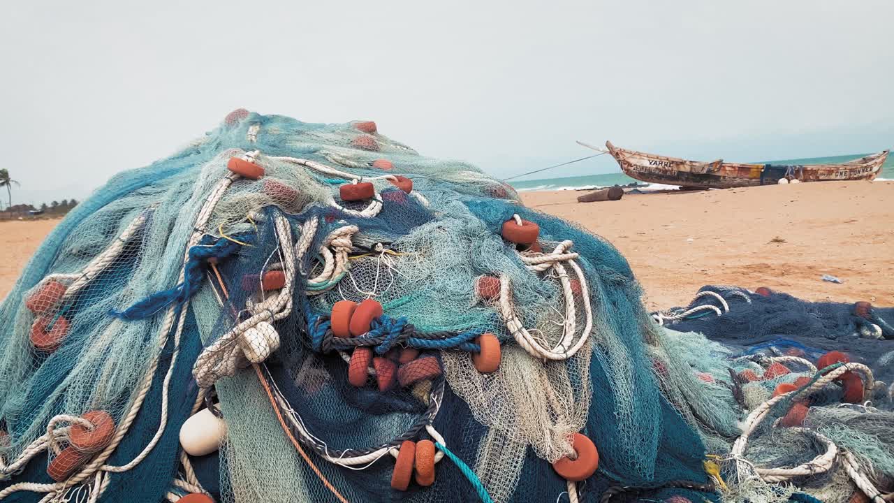 Rete da pesca e barca adagiate su una riva marina africana con l'oceano in lontananza