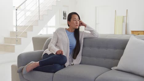 thoughtful asian woman sitting at sofa at home